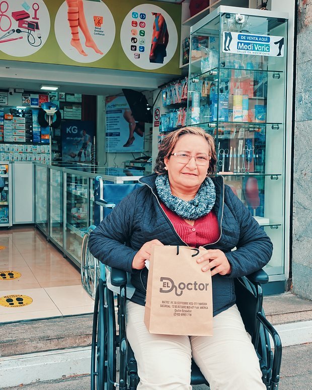 Una clienta en silla de ruedas con su compra, en la puerta del local